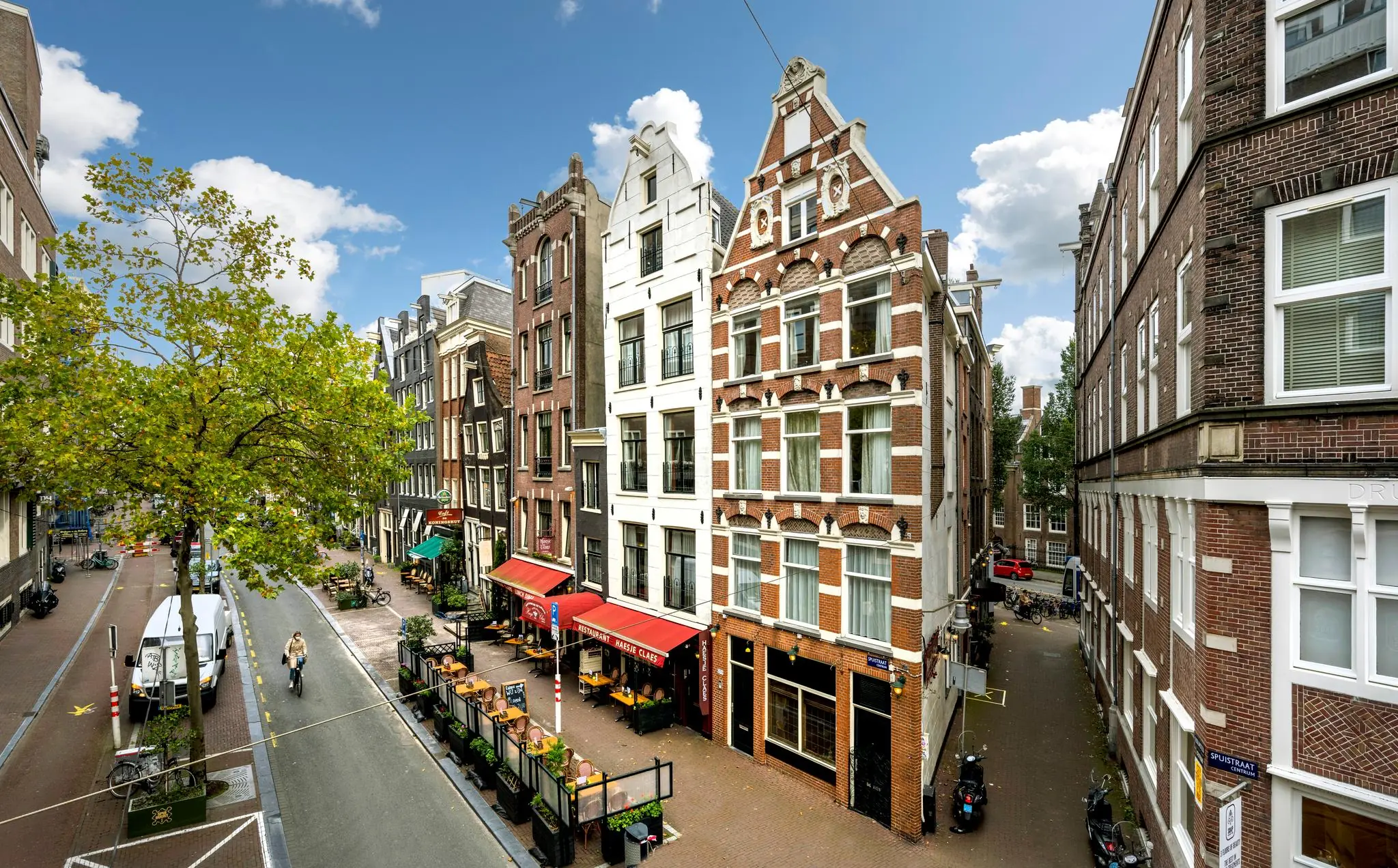 Gezellige straat met historische gevels, terrassen en een fietser op de Nieuwezijds Voorburgwal in Amsterdam.